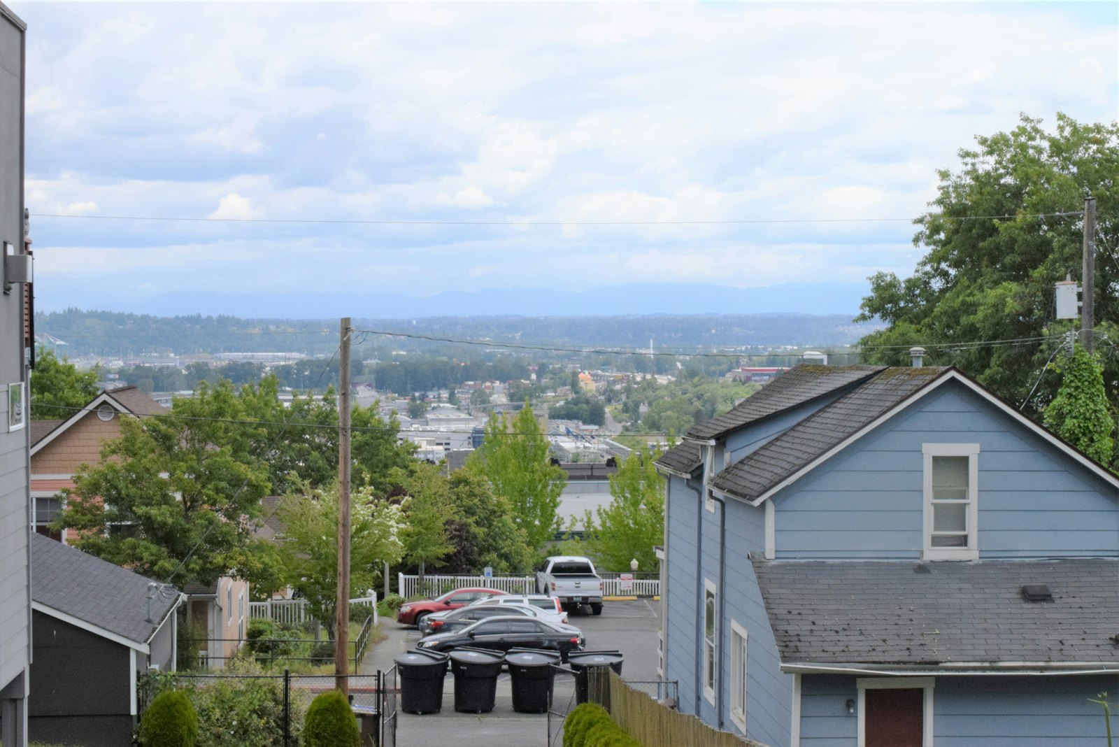 Blue lap-sided house on a hillside street overlooking a city and hills