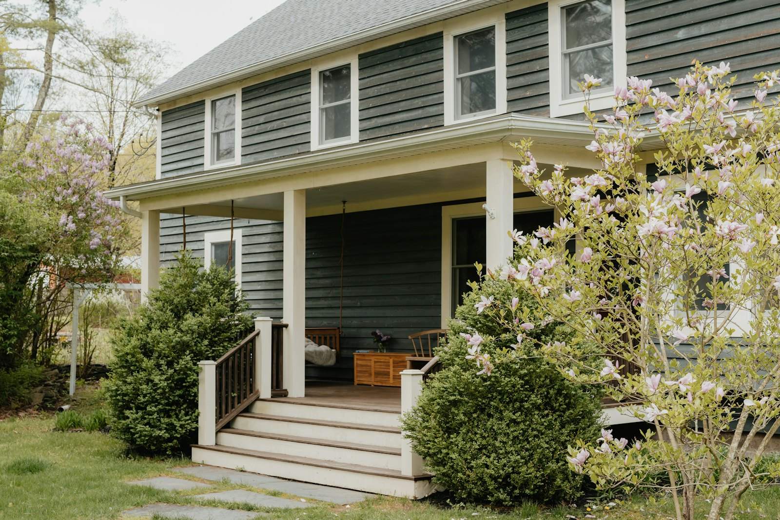 Gray lap-sided house with a white porch and a blooming tree