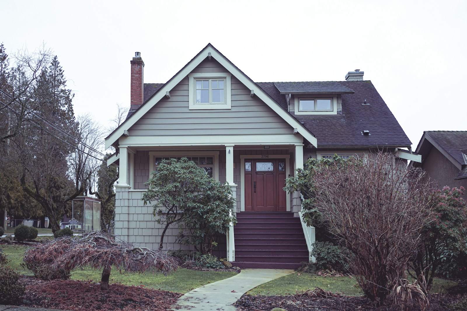 Green-gray Craftsman house with a red door and steps up to the porch