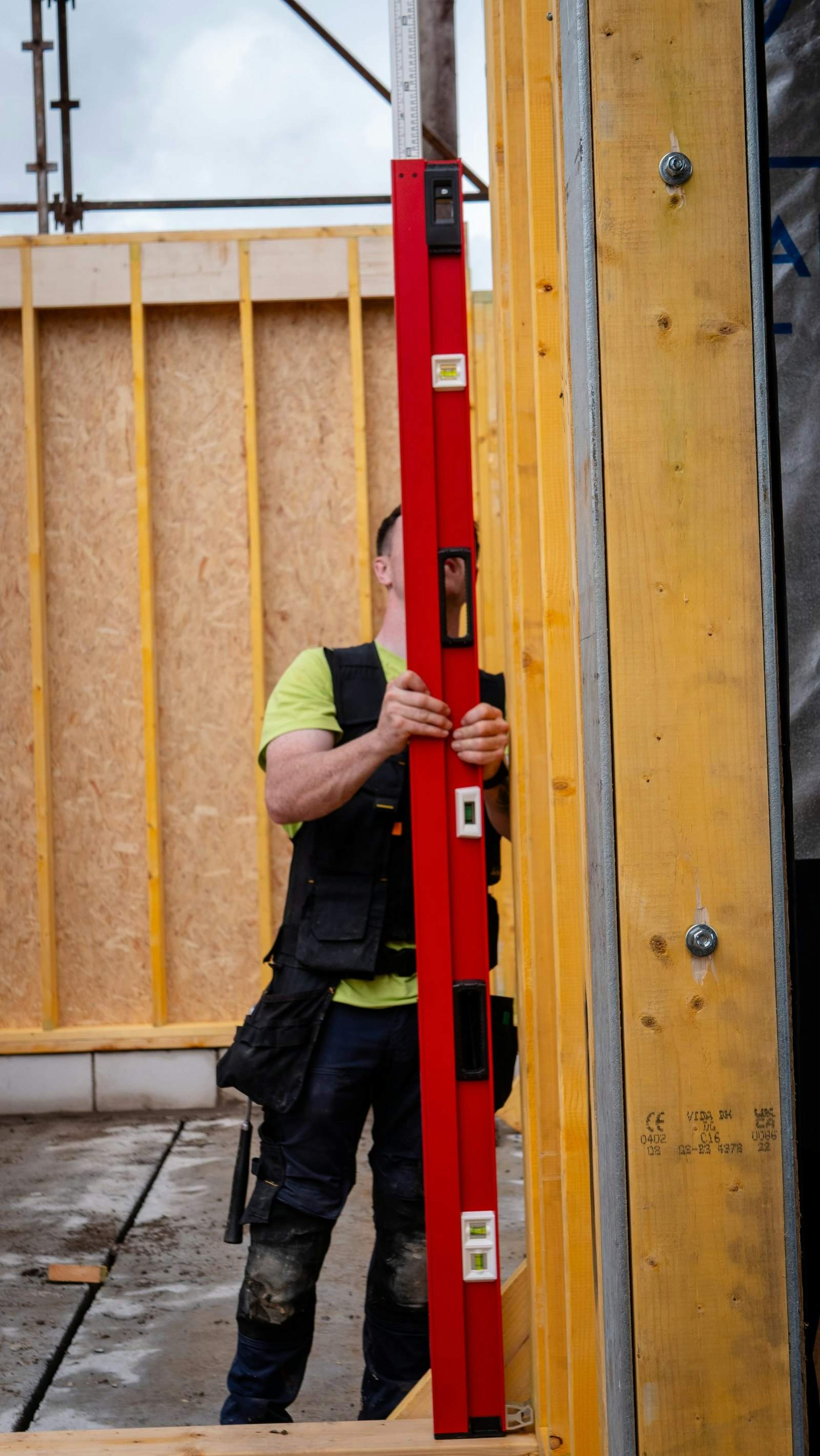 Construction worker holding a long level against a wooden wall