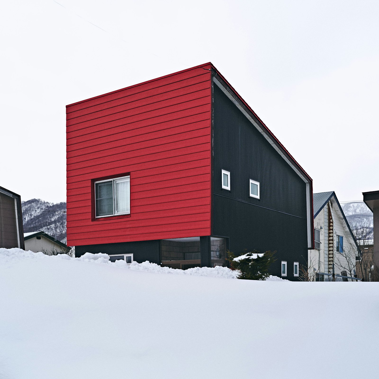 Modern house with red and black panel siding in snow