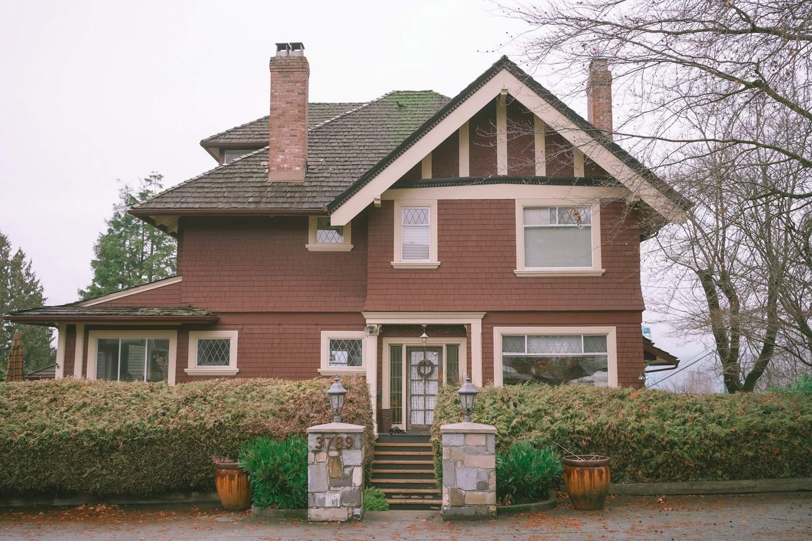 Red two-story Craftsman house with a hedge and stone gate posts