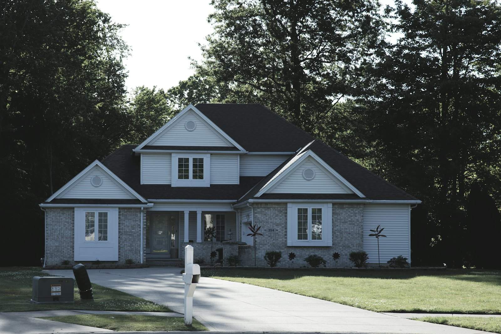 Suburban house with gray siding, a green lawn and tall trees