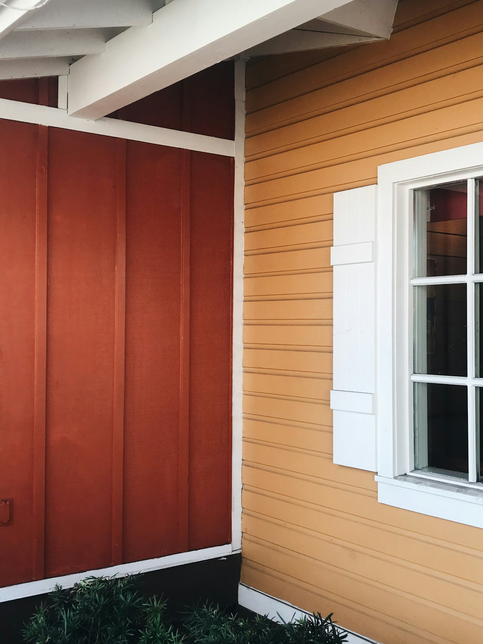 Red board-and-batten siding meeting orange lap siding beside a white-trimmed window